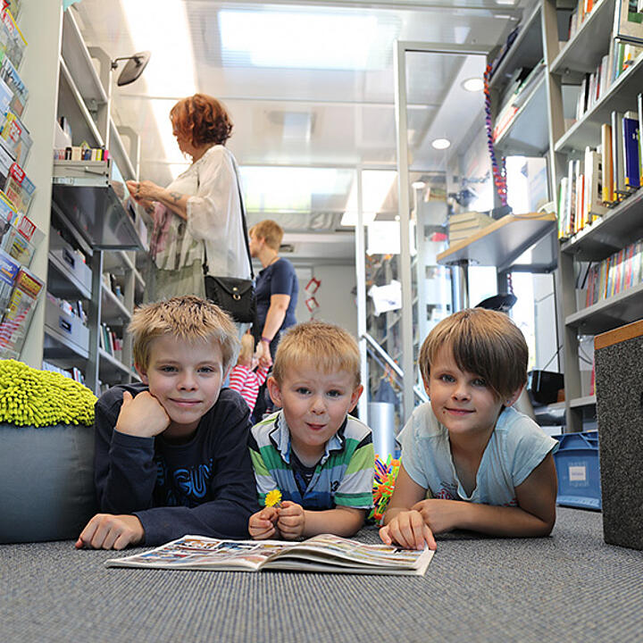 Kinder liegen auf dem Boden eines Bücherbuses und lesen Bücher.