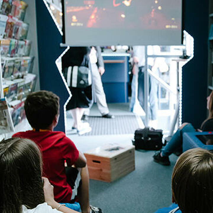 Kinder genießen eine Filmvorführung in einem Bücherbus, der mit Beamer und Leinwand ausgestattet ist.