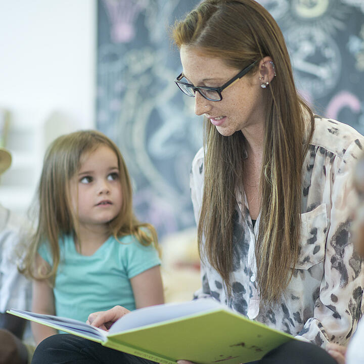 Eine junge Lehrerin liest Kindern aus einem Buch vor.