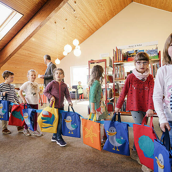 Kindern bilden eine Kette mit den Jutebeuteln des Projektes „LeseLachmöwe”.