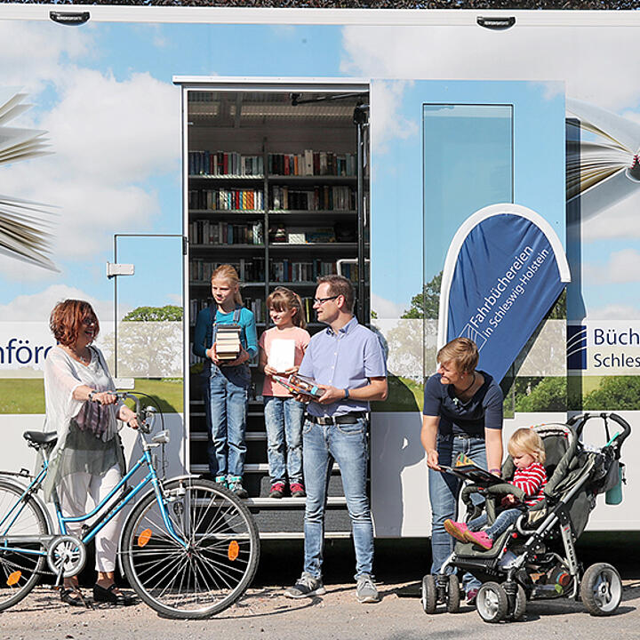 Menschen treffen sich vor der geöffneten Tür eines Bücherbusses.